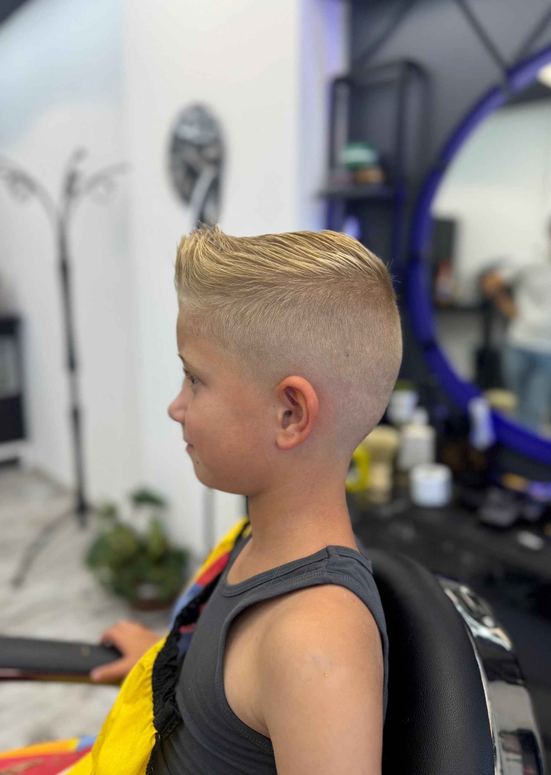 Jongen met quiff en skin fade, van opzij, voor de blauw verlichte ronde spiegel